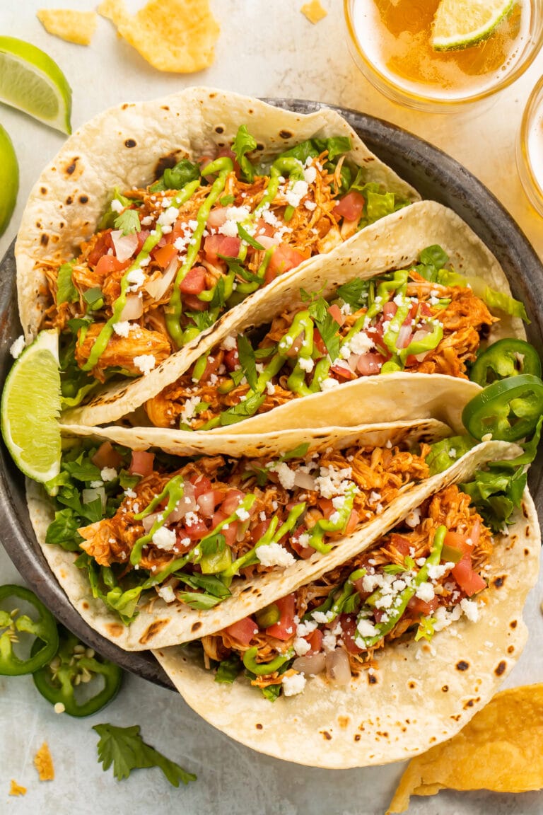 4 stuffed chicken tacos arranged on a plate. The tacos are filled with lettuce, tomato, cheese, and shredded chicken.