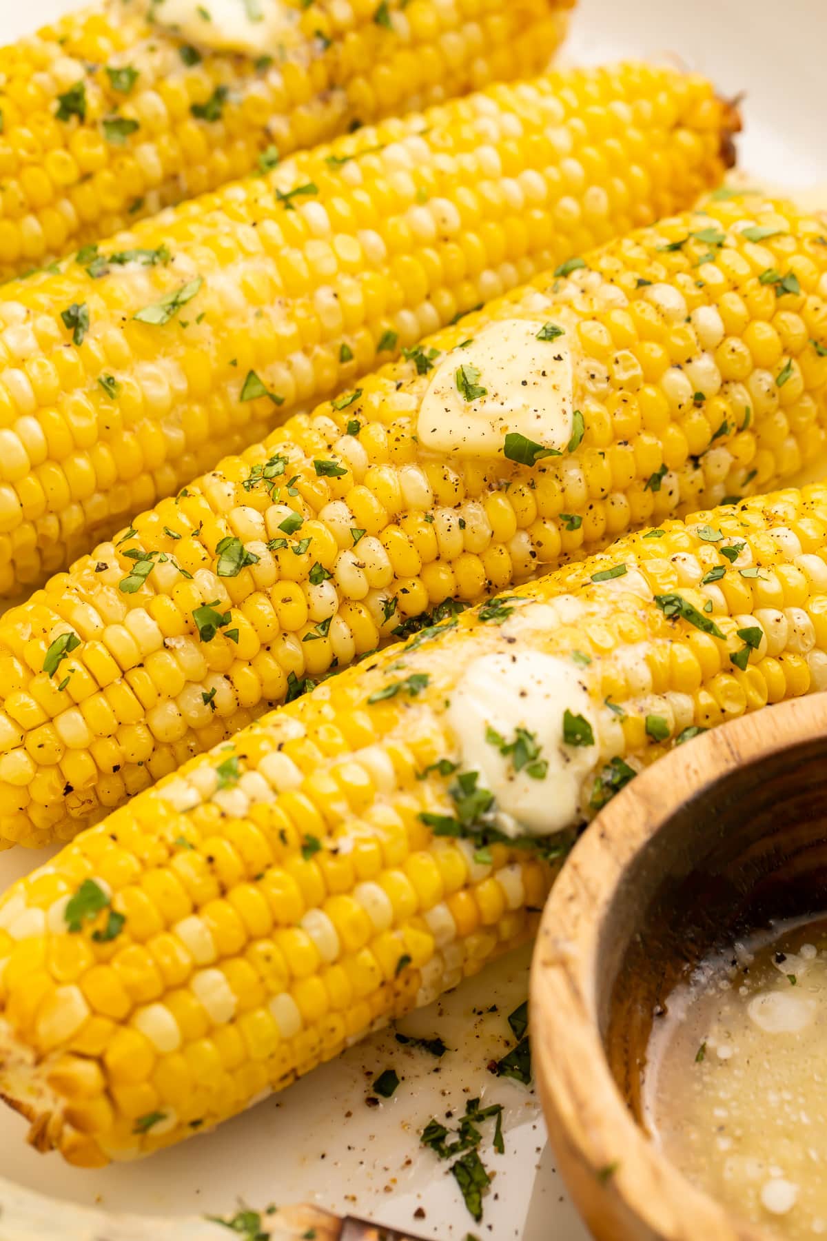 A close-up of 4 ears of air fryer corn on the cob topped with pats of butter and fresh parsley to garnish.