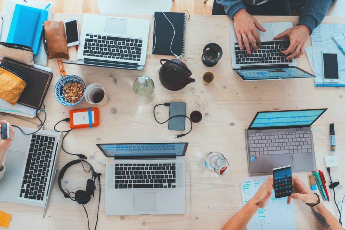 Laptops, phones, and tablets on a table with cups of coffee and people working.