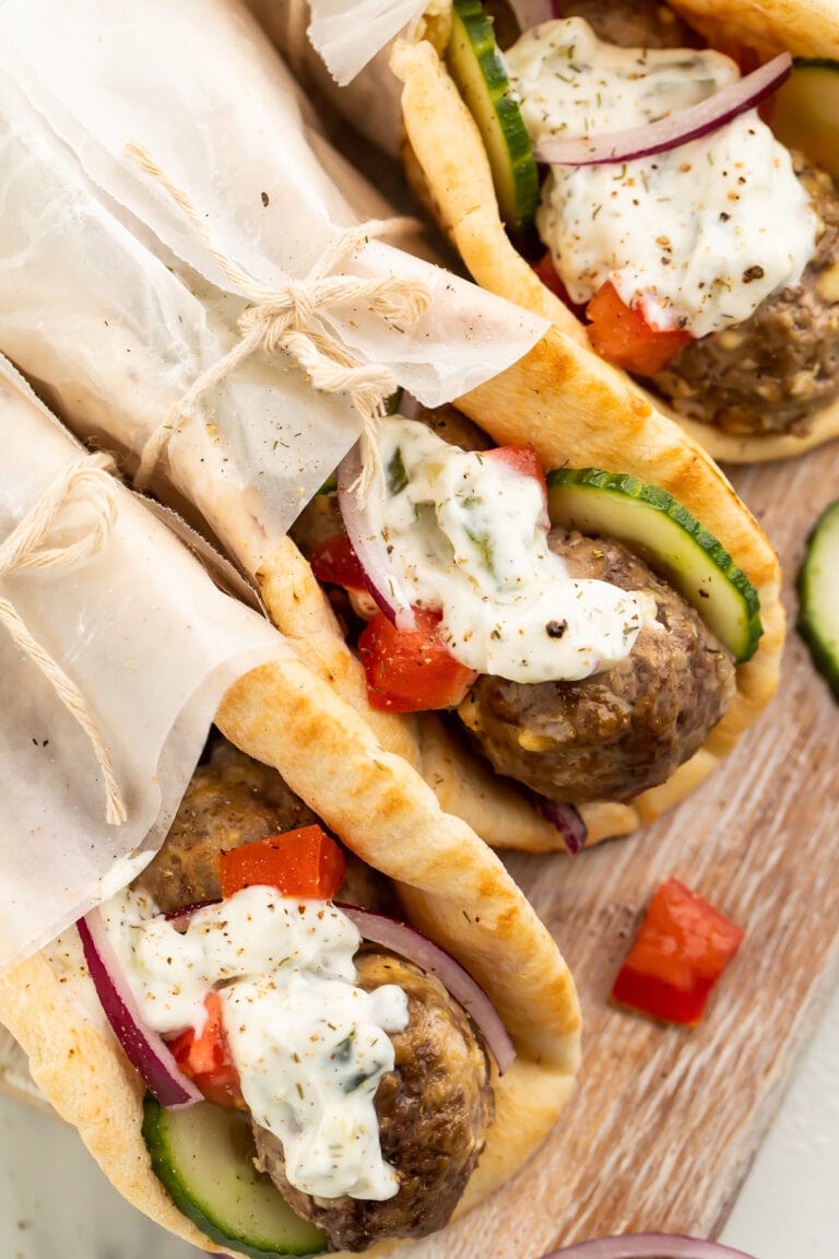 Three pitas stuffed with gyro meatballs, tzatziki, cucumber, and tomatoes, wrapped in parchment paper.