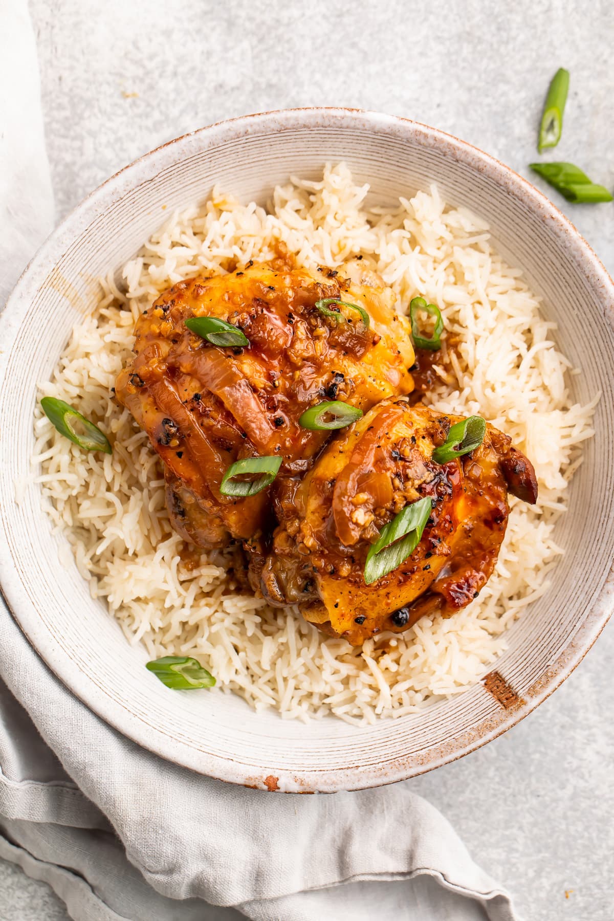 Instant Pot chicken adobo plated on a bed of rice in a large shallow bowl on a neutral table.