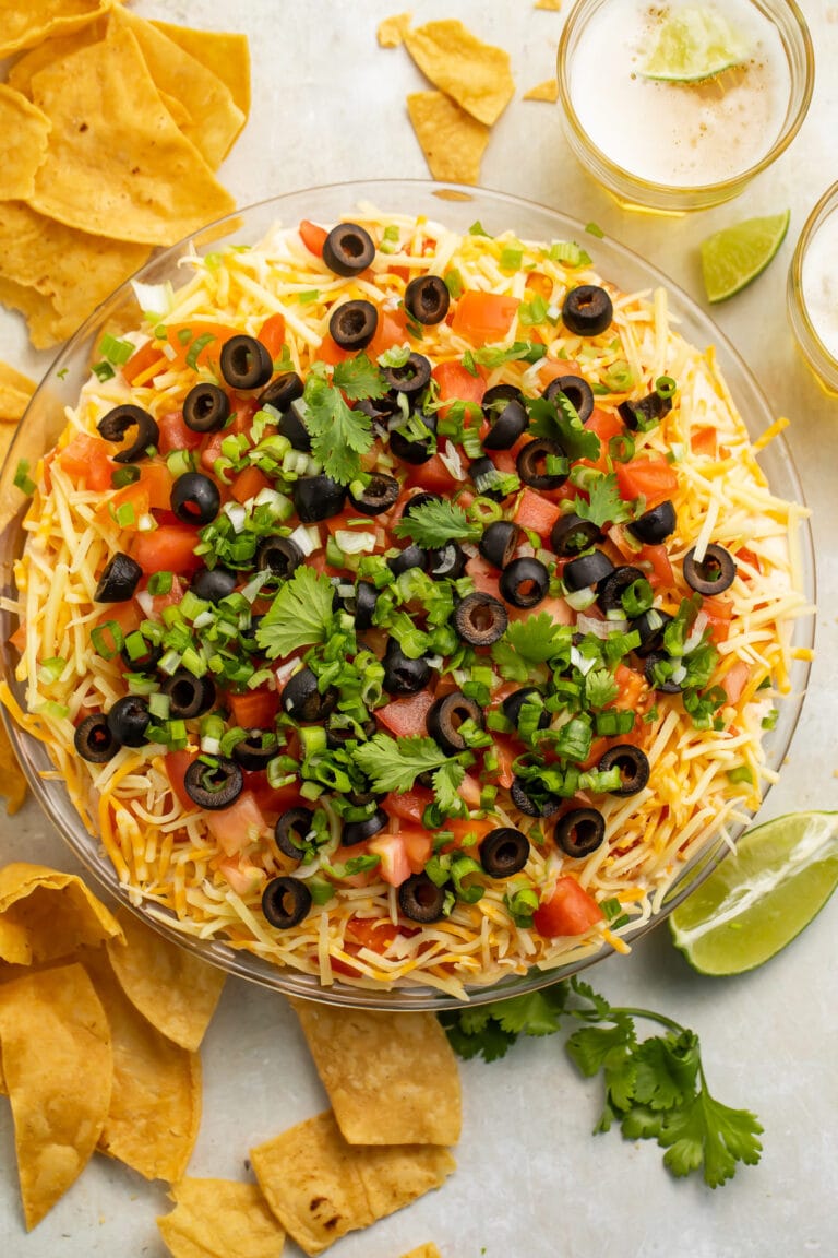 Top-down view of a large glass bowl filled with a 7 layer dip topped with green onions and olives.