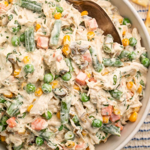 Top-down view of a bowl of Mexican chicken salad with shredded chicken, peas, carrots, and sour cream in a large bowl.