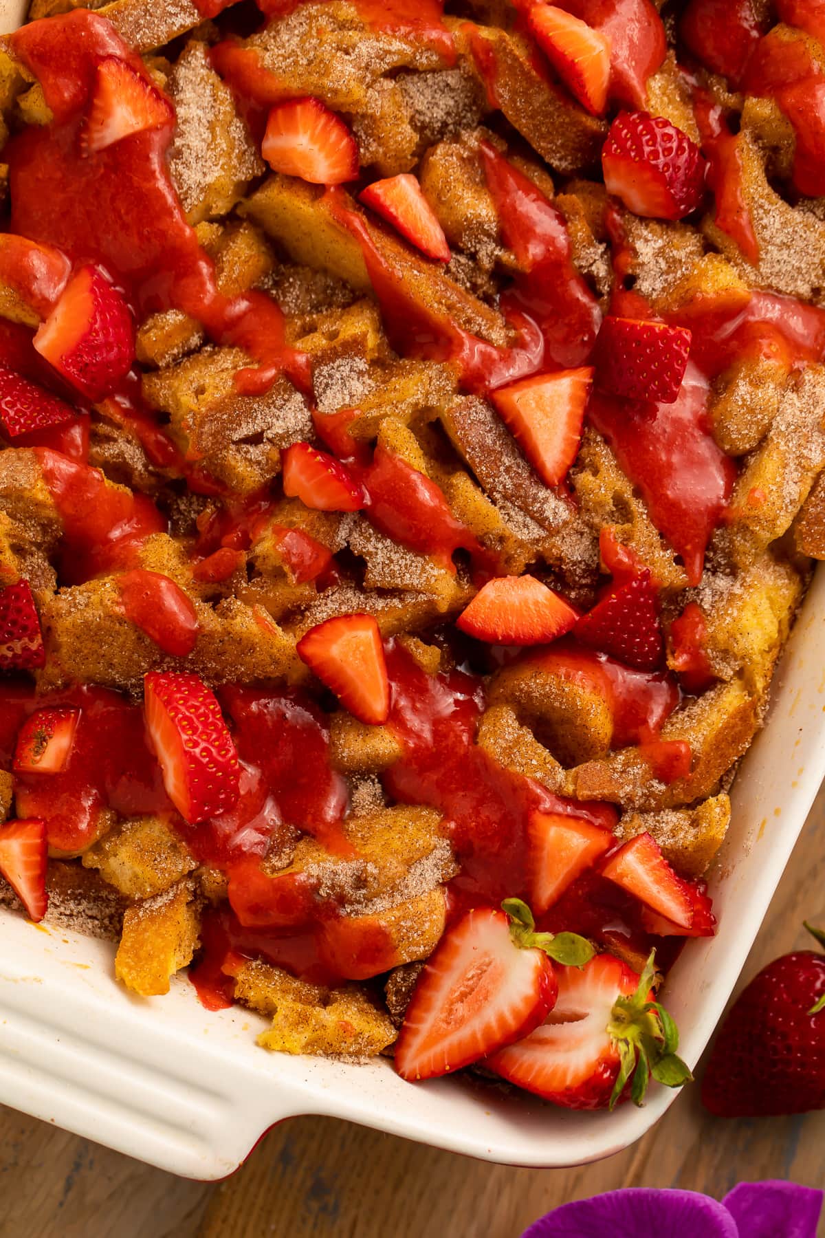 A casserole dish, angled on a table, filled with banana stuffed french toast casserole topped with strawberries.