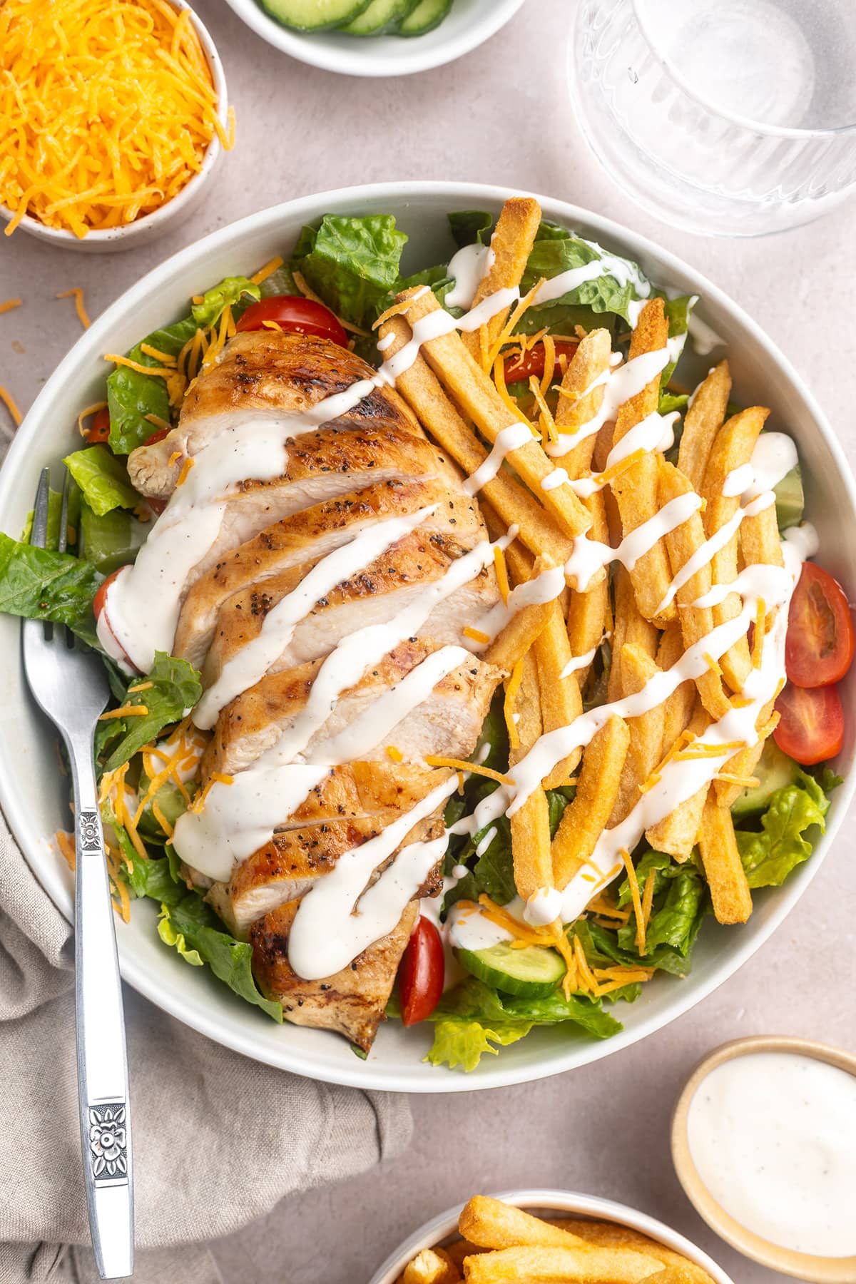 Zoomed out, top-down view of a Pittsburgh salad topped with sliced chicken, french fries, and ranch dressing.