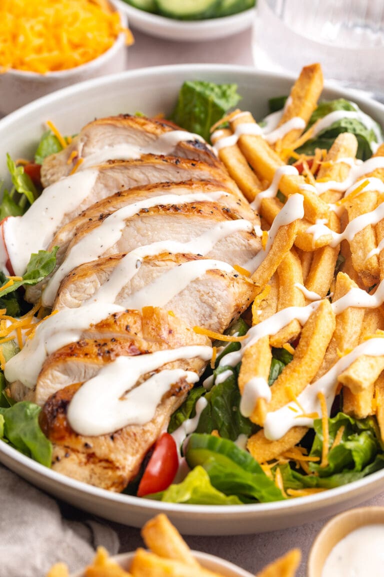 Angled view of a large bowl holding a Pittsburgh chicken salad with french fries and a drizzle of ranch dressing.