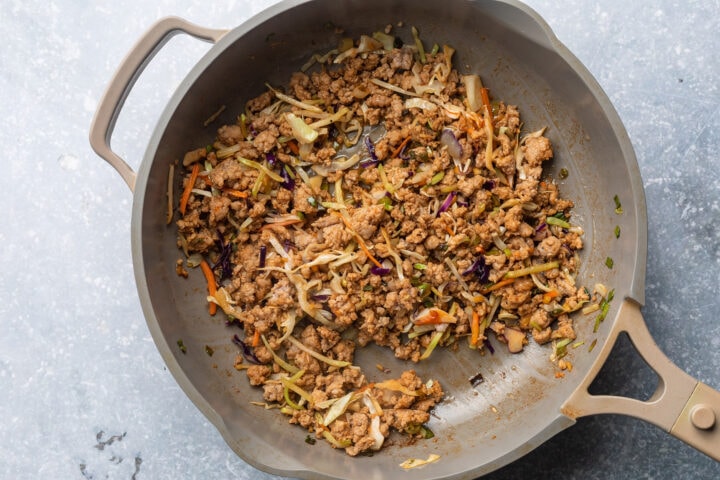 Prepared pork mixture for homemade egg rolls in a large skillet.