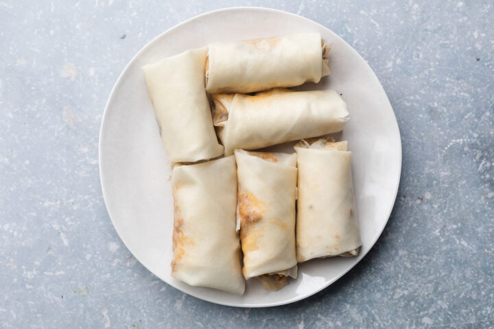 Fully wrapped, but not yet air fried, pork egg rolls in a large white plate.