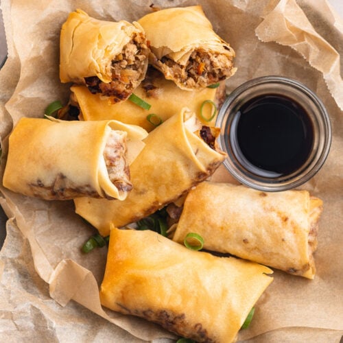 Top-down, overhead view of homemade air fryer egg rolls on a plate lined with parchment paper next to a small bowl of soy sauce.