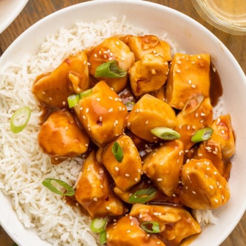 Orange glazed Instant Pot honey garlic chicken garnished with sesame seeds and sliced green onions in a bowl with white rice.