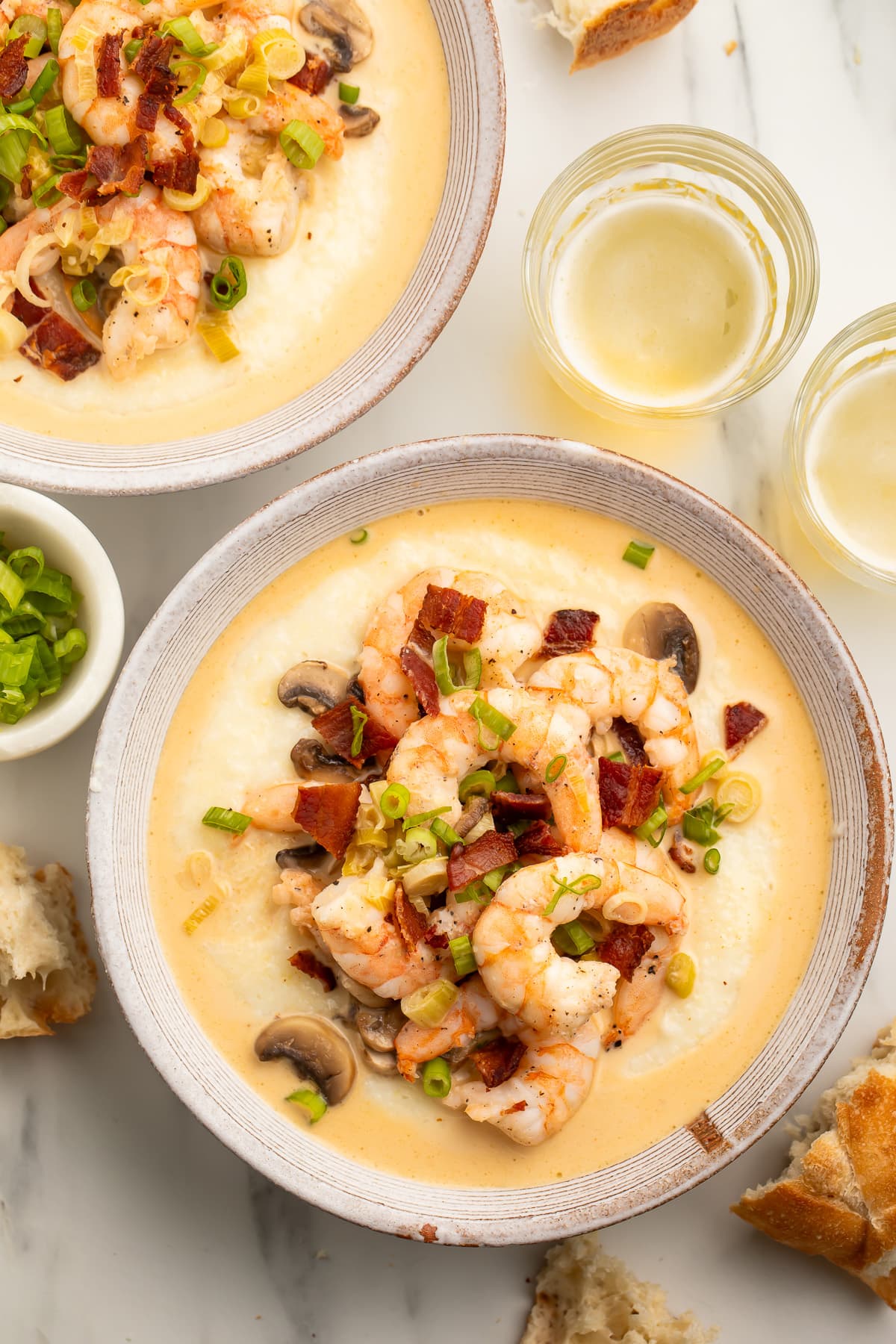 Overhead view of a large white bowl holding creamy grits topped with pink shrimp, bacon, and mushrooms.