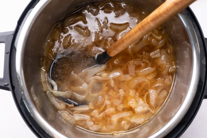 Sliced, caramelized onions in the bottom of an Instant Pot with beef broth.