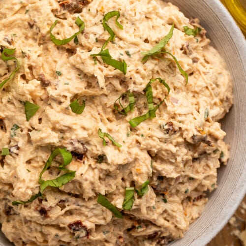 A close-up look at a large neutral bowl holding marry me chicken salad, with sun dried tomatoes and fresh basil.