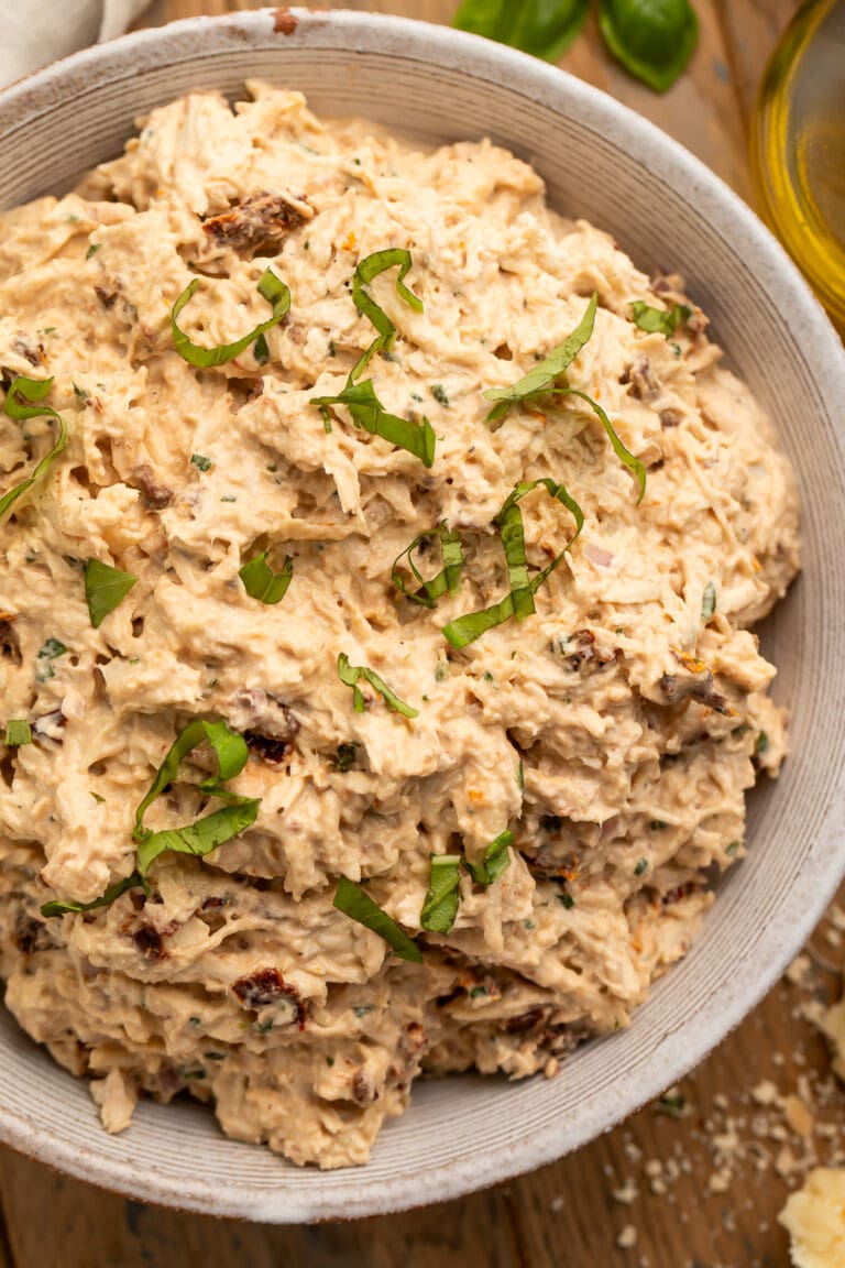 A close-up look at a large neutral bowl holding marry me chicken salad, with sun dried tomatoes and fresh basil.