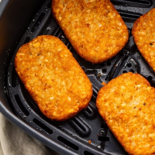 4 frozen hash brown patties in an air fryer basket, cooked until golden and crispy.