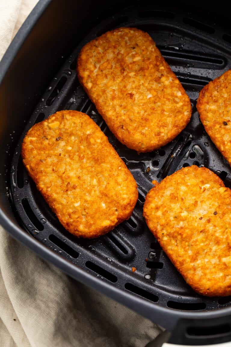 4 frozen hash brown patties in an air fryer basket, cooked until golden and crispy.