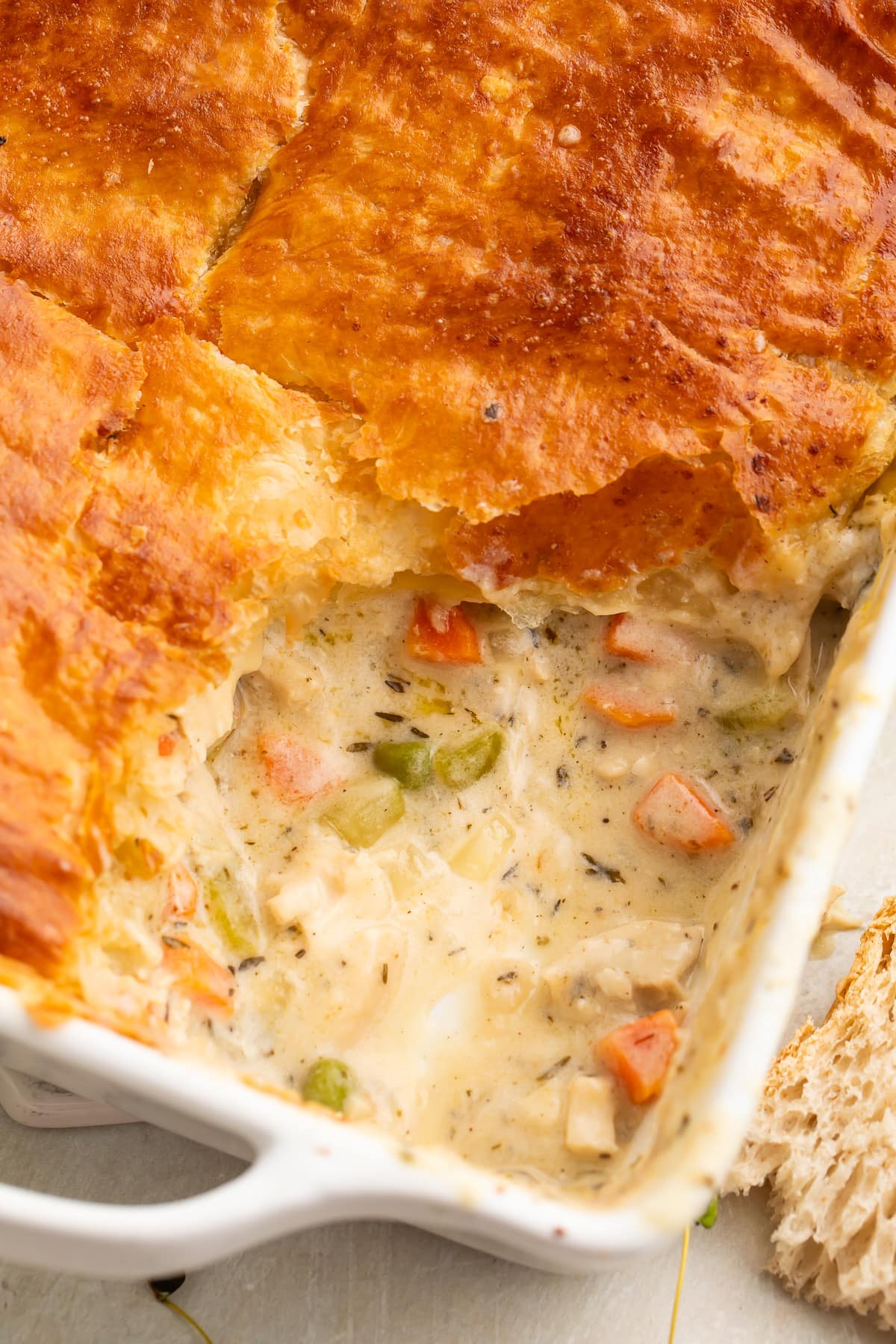 Chicken pot pie casserole in a square dish, with a corner scooped out to show some of the filling.