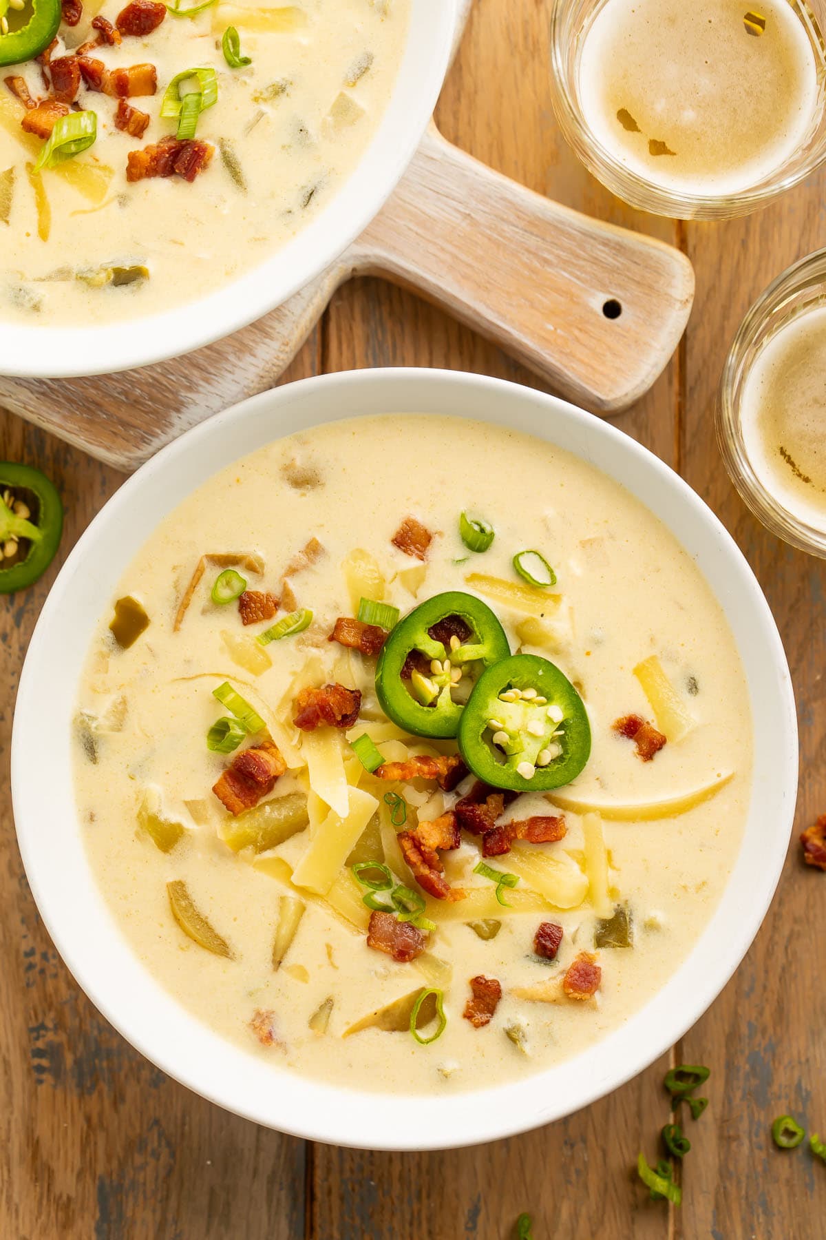 Overhead view of 2 large white bowls holding pale yellow jalapeño popper soup on a wooden table.