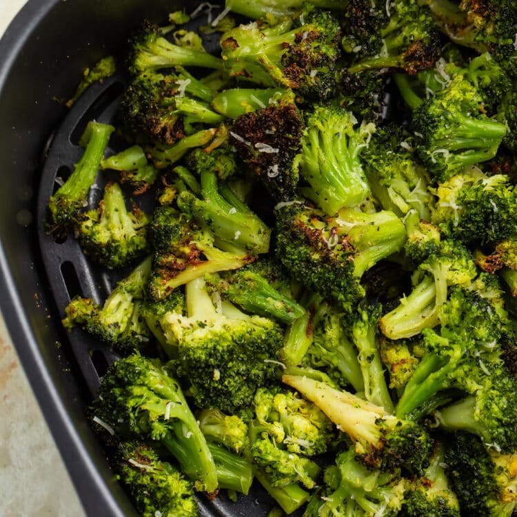 Previously frozen broccoli florets, resting in an air fryer basket after being cooked until some spots are dark brown and crisp.