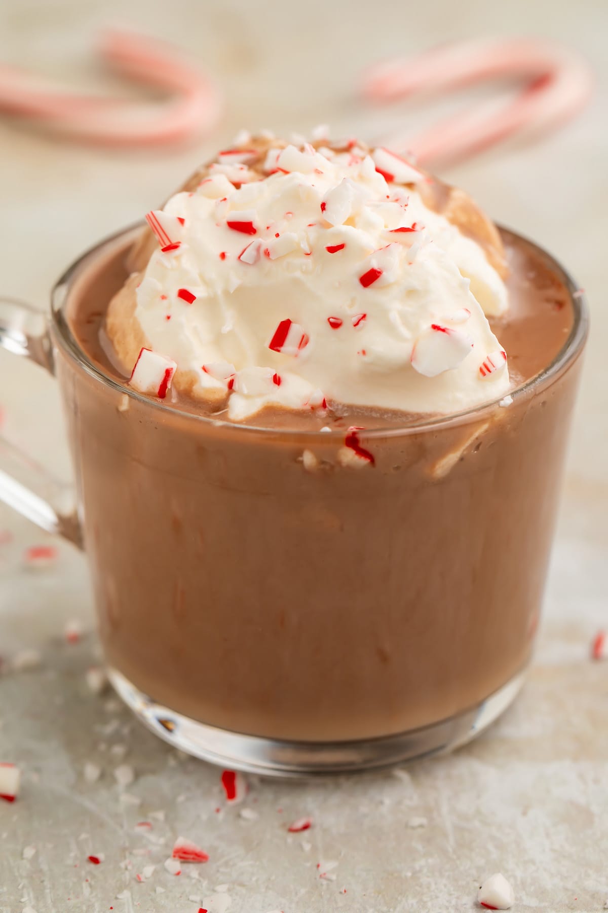 A clear glass mug of rich paleo peppermint hot chocolate topped with whipped coconut cream and candy cane pieces.