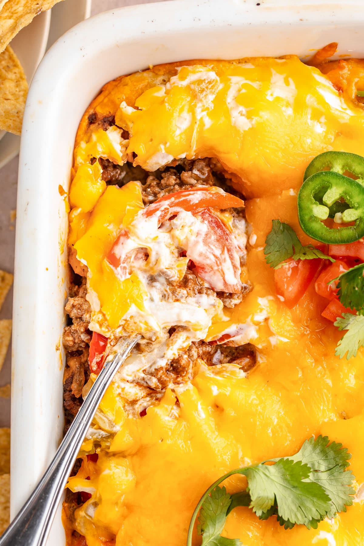 Close-up of a spoon, holding a scoop of John Wayne casserole, resting in a casserole dish of John Wayne casserole.