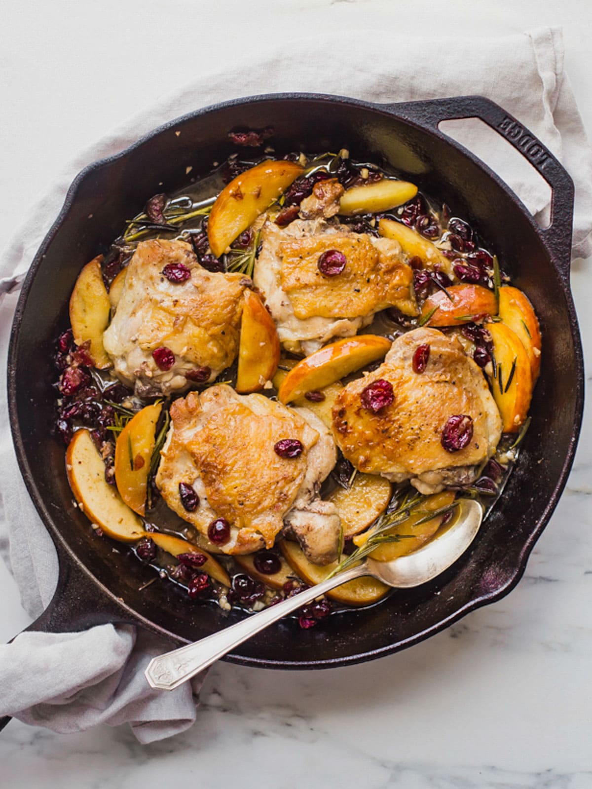 Overhead photo showing 4 medium chicken thighs in a cast iron skillet with a paleo cranberry apple sauce.