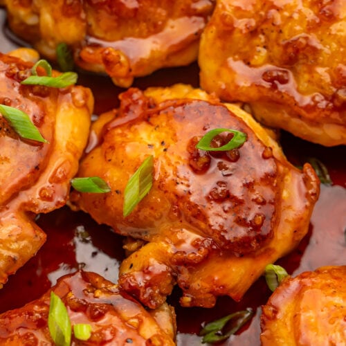 Honey sriracha chicken thighs resting in a large silver skillet with honey sriracha sauce.