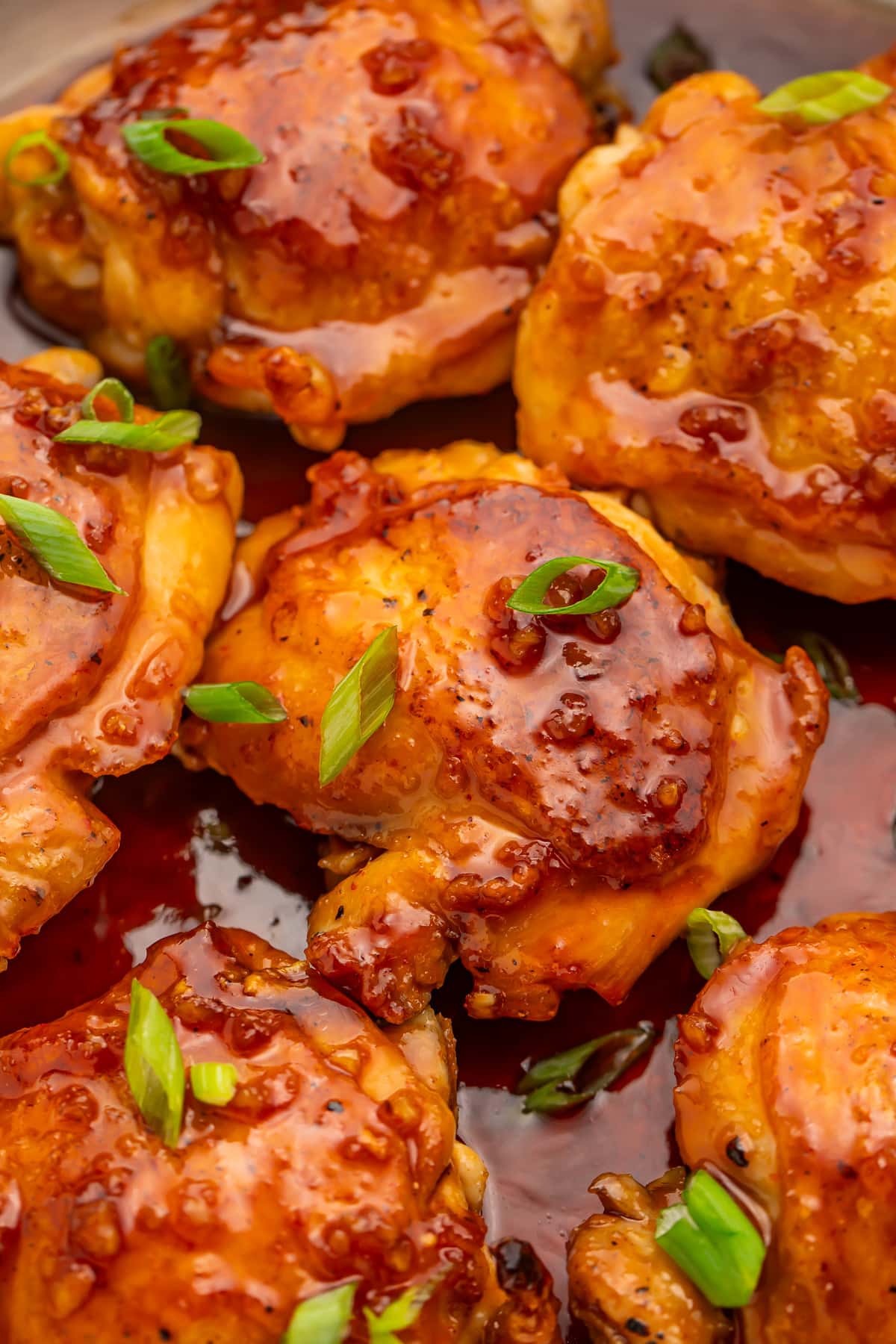 Honey sriracha chicken thighs resting in a large silver skillet with honey sriracha sauce.