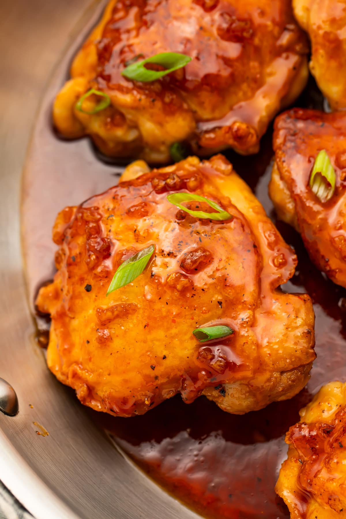 Honey sriracha chicken thighs resting in a large silver skillet with honey sriracha sauce.