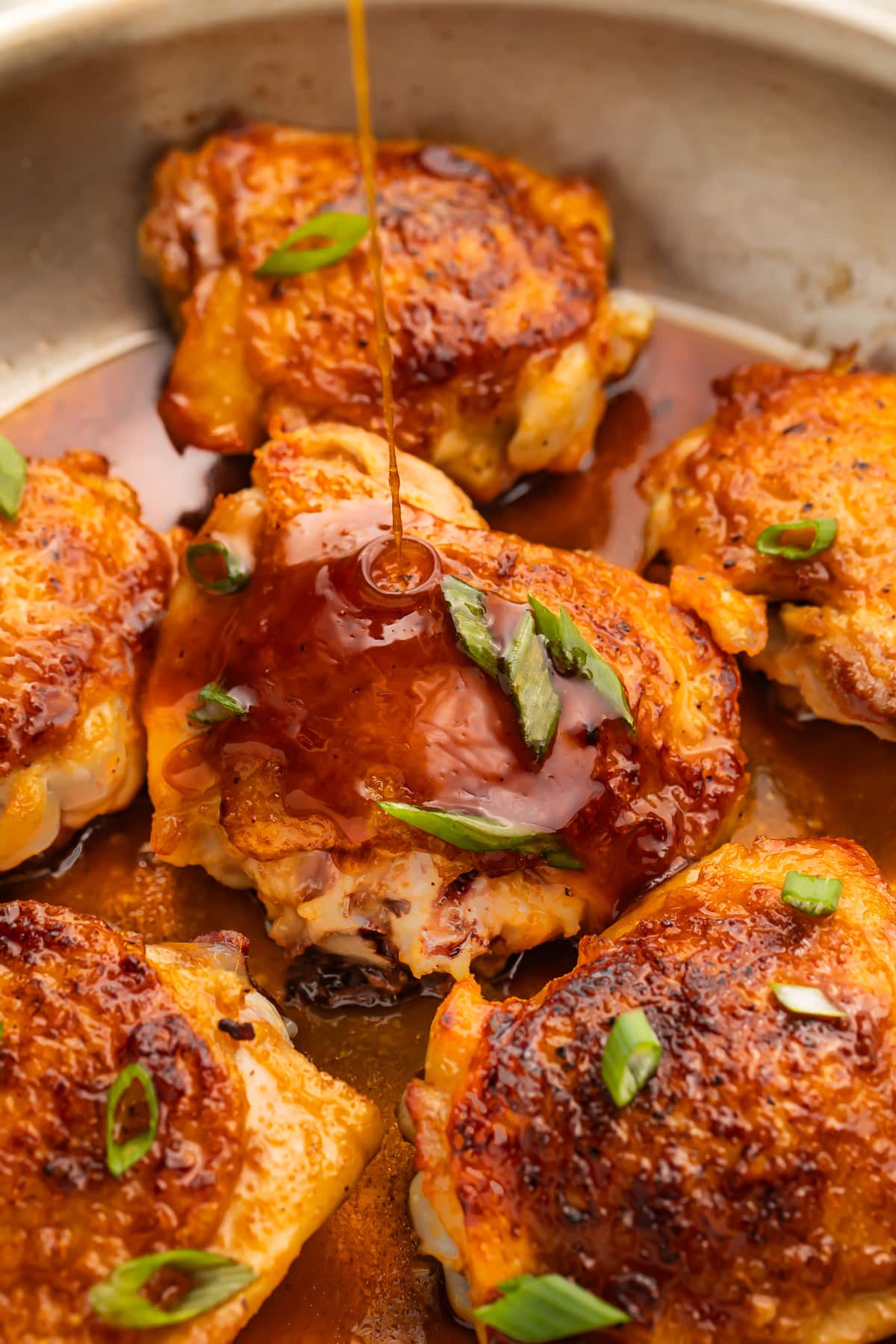 Hot honey sauce being poured over crispy chicken thighs in a large silver skillet.