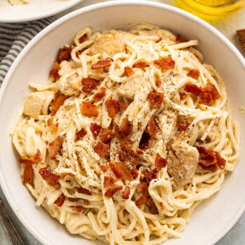 A large white bowl of paleo carbonara made with palmini, dairy-free Alfredo sauce, and compatible bacon.