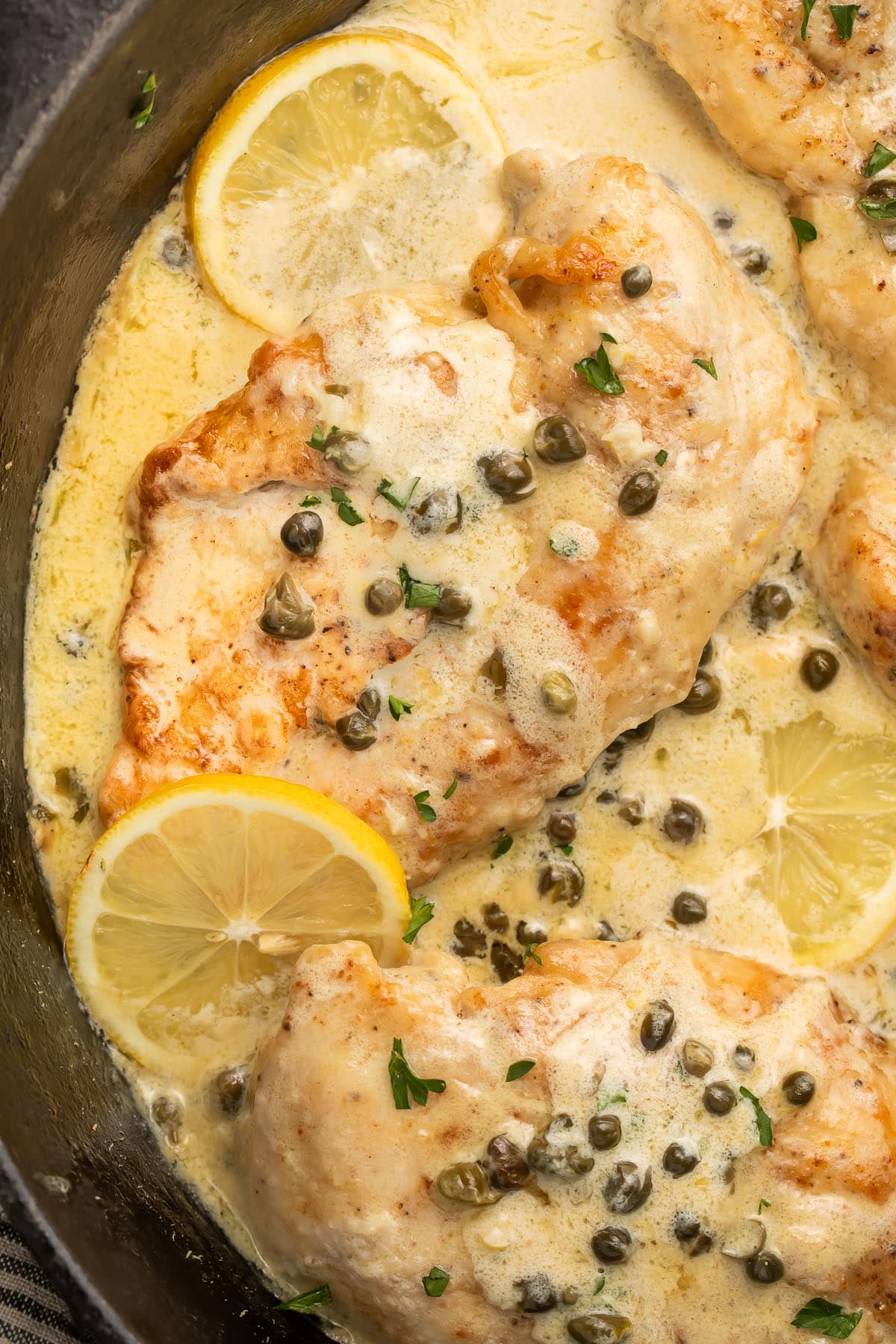 A cast-iron skillet holding creamy chicken piccata with lemon sauce and capers.