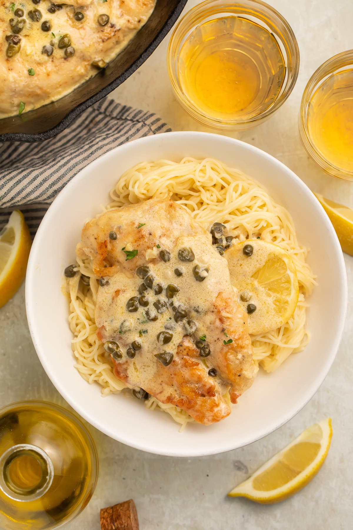 Chicken piccata plated with pasta and capers.