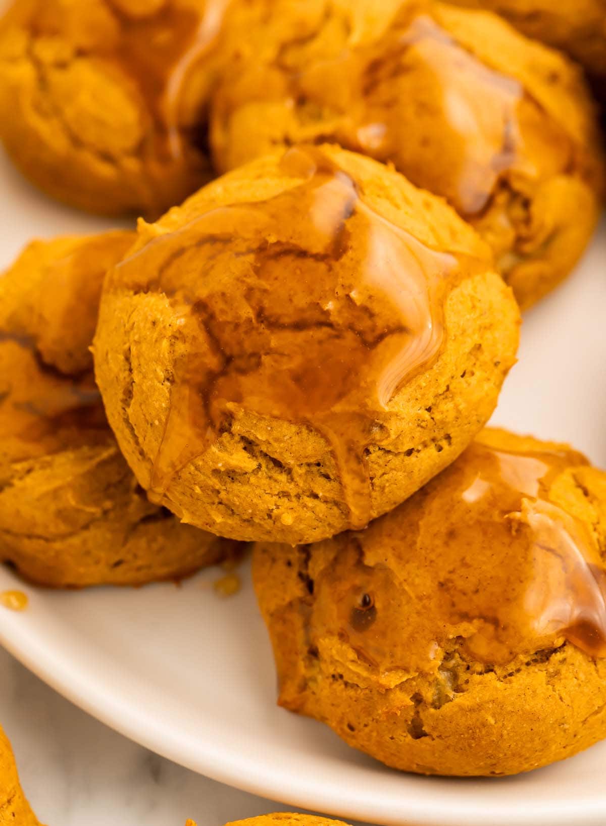 Pumpkin cookies topped with a light maple glaze arranged on and around a round white plate on a table.