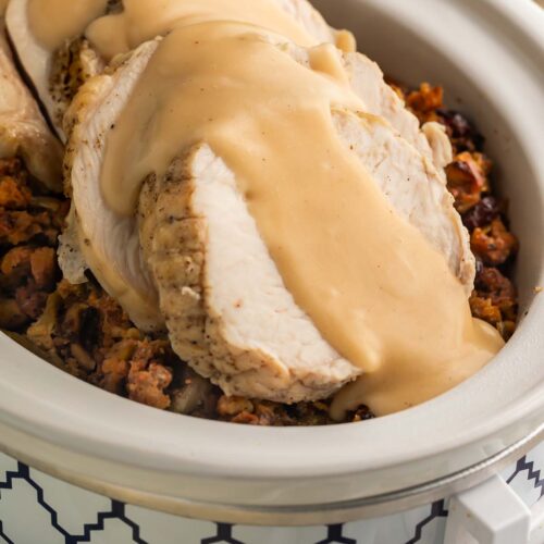 Close-up of thick slices of turkey, smothered in gravy, on top of cooked stuffing and green beans in a Crockpot.