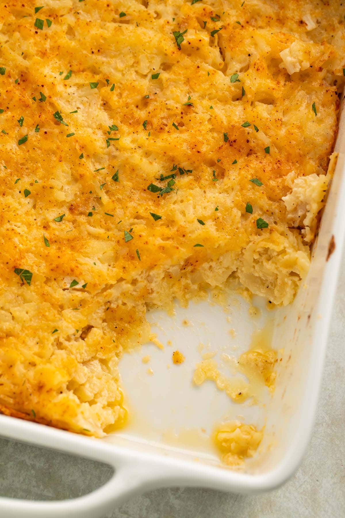 A large spoonful of cheesy potato casserole removed from the corner of a square white casserole dish.