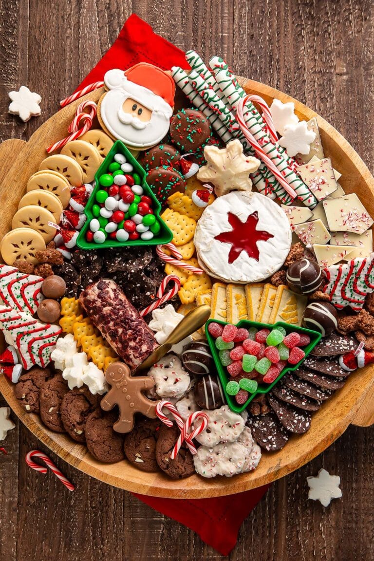 A Christmas dessert themed grazing board, packed full with Christmas tree cakes, brie, goat cheese, crackers, pretzels, truffles, nuts, cookies, and other holiday-themed treats.